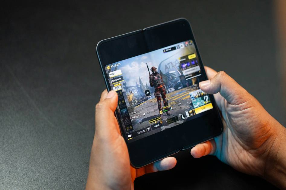 Mobile gamer holding a smartphone playing a battle royale game with dynamic in-game action overlay
